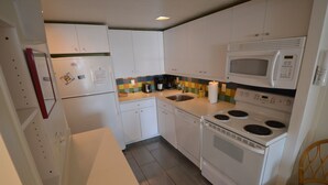 Une cuisine de taille réduite, avec des meubles blancs, un four à micro-ondes, une cuisinière, un évier et un réfrigérateur.