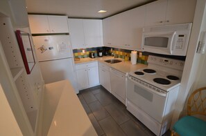 A compact kitchen with white cabinets, a microwave, a stove, a sink, and a refrigerator. - Edgewater House - Ocean Front Units With Spectacular Views! (Rehoboth Beach)