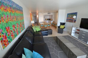 A living room with a sofa, ottoman, and a large abstract painting on the wall.