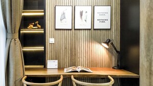 Ein Holztisch mit zwei Stühlen, einer Lampe und einem Buch. An der Wand befinden sich gerahmte Bilder und auf dem Tisch ein Kalender.