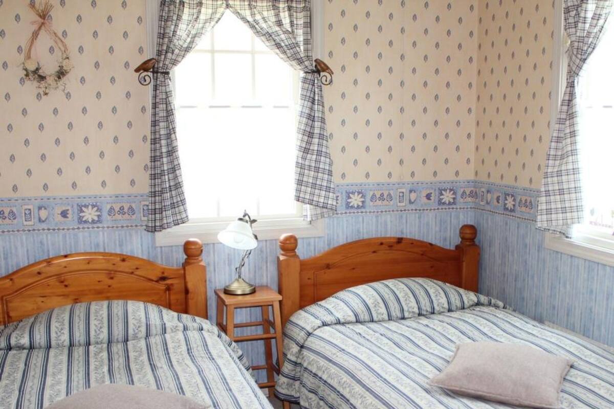 Un dormitorio con dos camas de madera, cada una con ropa de cama y almohadas a rayas. Hay una mesita de noche pequeña con una lámpara entre las camas.