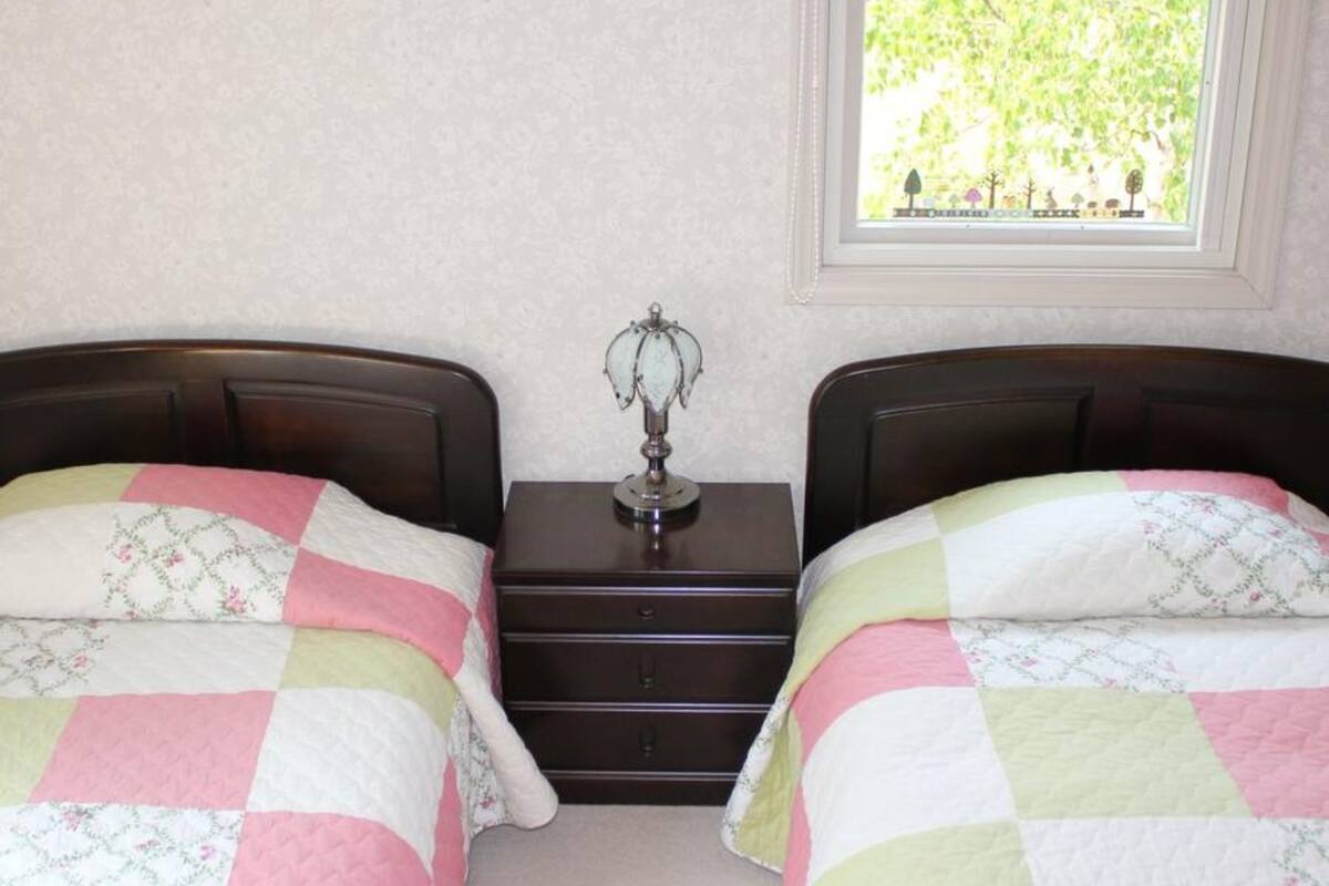 Un dormitorio con dos camas, cada una con colcha acolchada, una mesita de noche entre ellas y una ventana con vistas a zonas verdes.