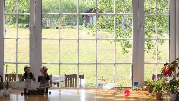 A room with large windows offering a view of a grassy yard and a distant building. - Rusutsu Pension Clydesdale (Rusutsu)