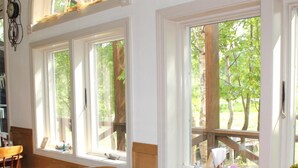 A dining area with a wooden table and chairs, large windows with a view of trees and a deck outside. - Rusutsu Pension Clydesdale (Rusutsu)