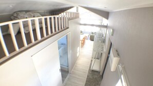 A narrow hallway with a loft bedroom above, a white door, and a small kitchen area with a refrigerator and a chair. - Rusutsu Pension Clydesdale (Rusutsu)