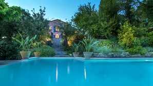 Une piscine avec un escalier en pierre menant à une maison entourée d’une végétation luxuriante.