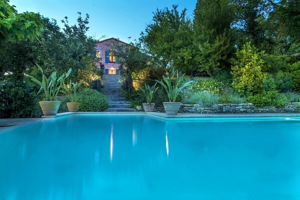 A swimming pool with a stone staircase leading to a house surrounded by lush greenery.