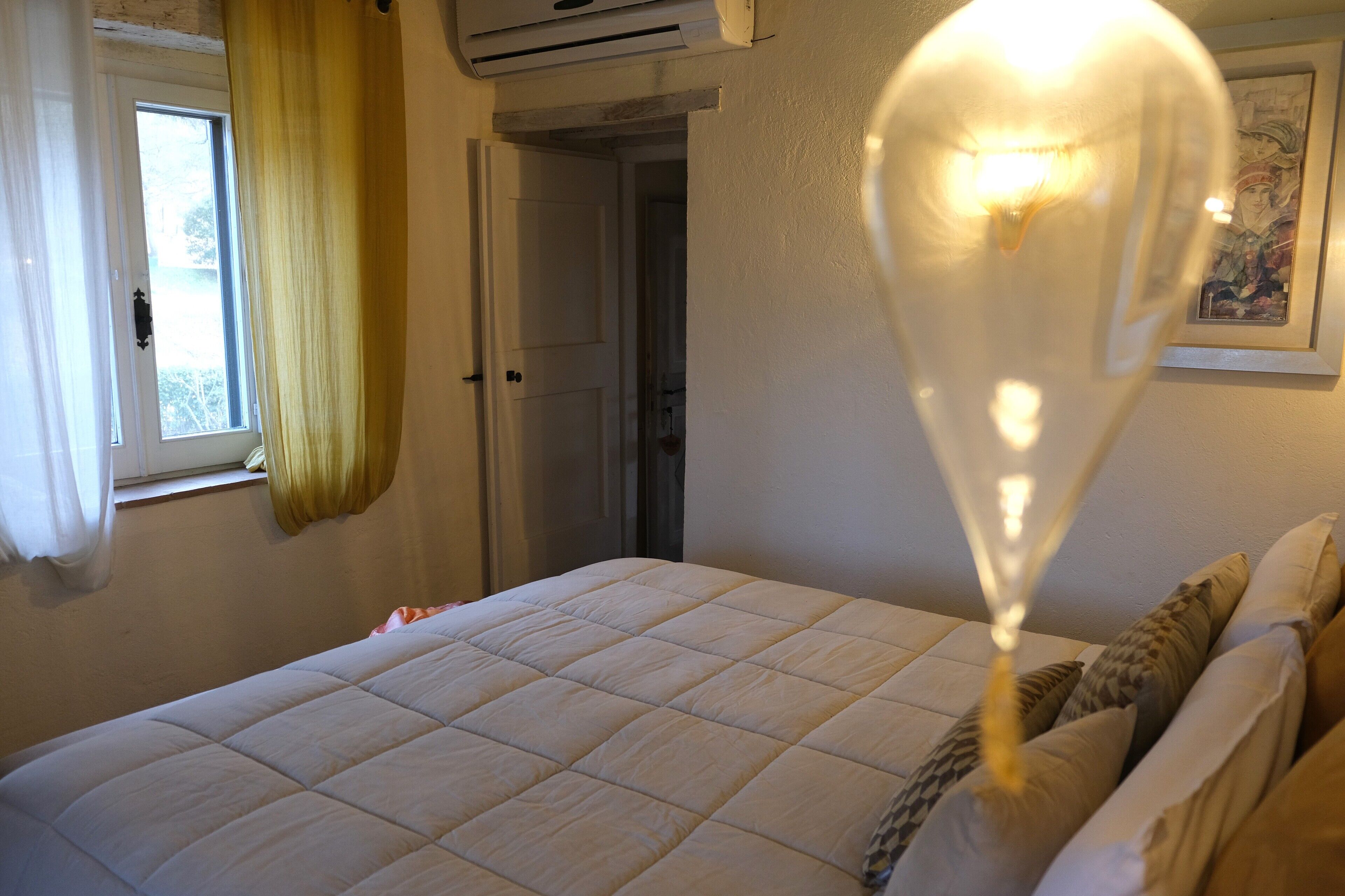 A bedroom with a bed, a window with curtains, and a wall-mounted air conditioner.