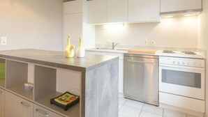 A modern kitchen with white cabinets, a stainless steel stove, and a central island with a cutting board. - Polderhuis 78 parking and shared pool by Interhome (De Haan)