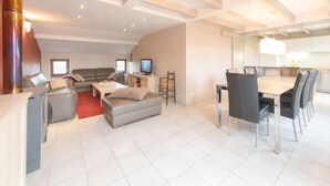 A spacious living area with a sofa set, a dining table with chairs, a television, and a kitchen area with cabinets and a countertop. - Polderhuis 78 parking and shared pool by Interhome (De Haan)