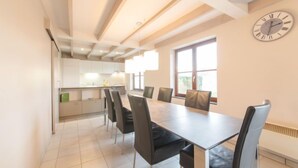 A modern kitchen with white cabinets and a central island, a dining area with a large table and chairs, and a clock on the wall. - Polderhuis 78 parking and shared pool by Interhome (De Haan)