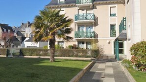 Un edificio de varios pisos con fachada simétrica, una entrada central y un pequeño jardín con una palmera.