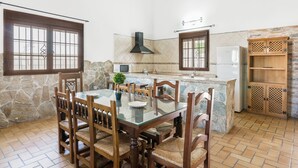 A kitchen with a dining table, chairs, a stove, a refrigerator, and a stone wall. - Rustic Villa Close to Beach with Pool, Terrace & Wi-Fi; Pets Allowed, Parking Available (Conil de la Frontera)