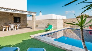 A pool with a stone border, a green lawn, and a white building with a stone facade. - Rustic Villa Close to Beach with Pool, Terrace & Wi-Fi; Pets Allowed, Parking Available (Conil de la Frontera)