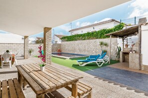 A patio area with a wooden table, lounge chairs, a small pool, and a stone wall.
