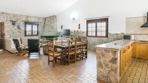 A spacious living area with a stone wall, a dining table with chairs, a sofa, a TV, and a kitchen area with a microwave. - Rustic Villa Close to Beach with Pool, Terrace & Wi-Fi; Pets Allowed, Parking Available (Conil de la Frontera)