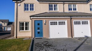 A two-story residential building with a beige exterior, a blue door, and two garage doors. - Devonvale Place by Interhome (Kinross)