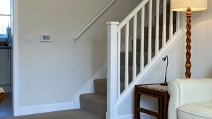A living room with a beige carpet, a white sofa, a wooden side table, a lamp, and a staircase with white railings. - Devonvale Place by Interhome (Kinross)