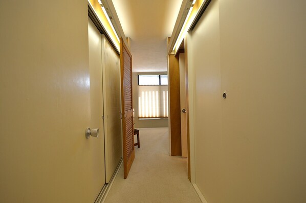 A narrow hallway with carpeted floors, wooden doors, and a window with blinds.