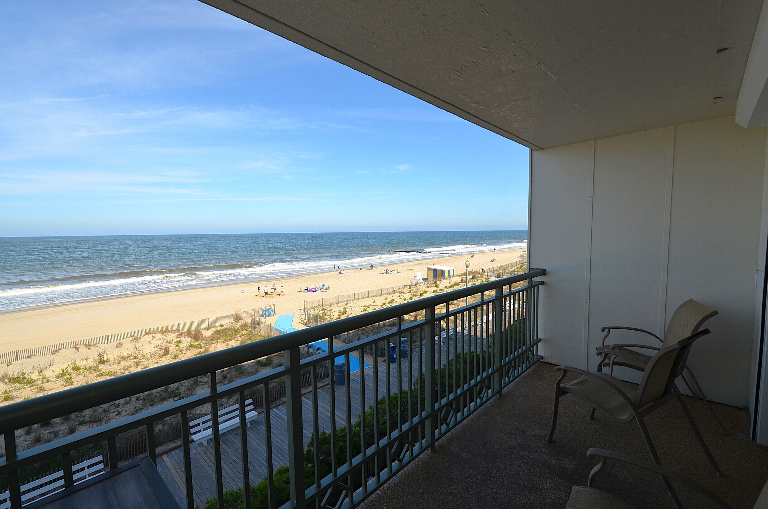 A balcony with a view of the beach, a chair, and a small table.