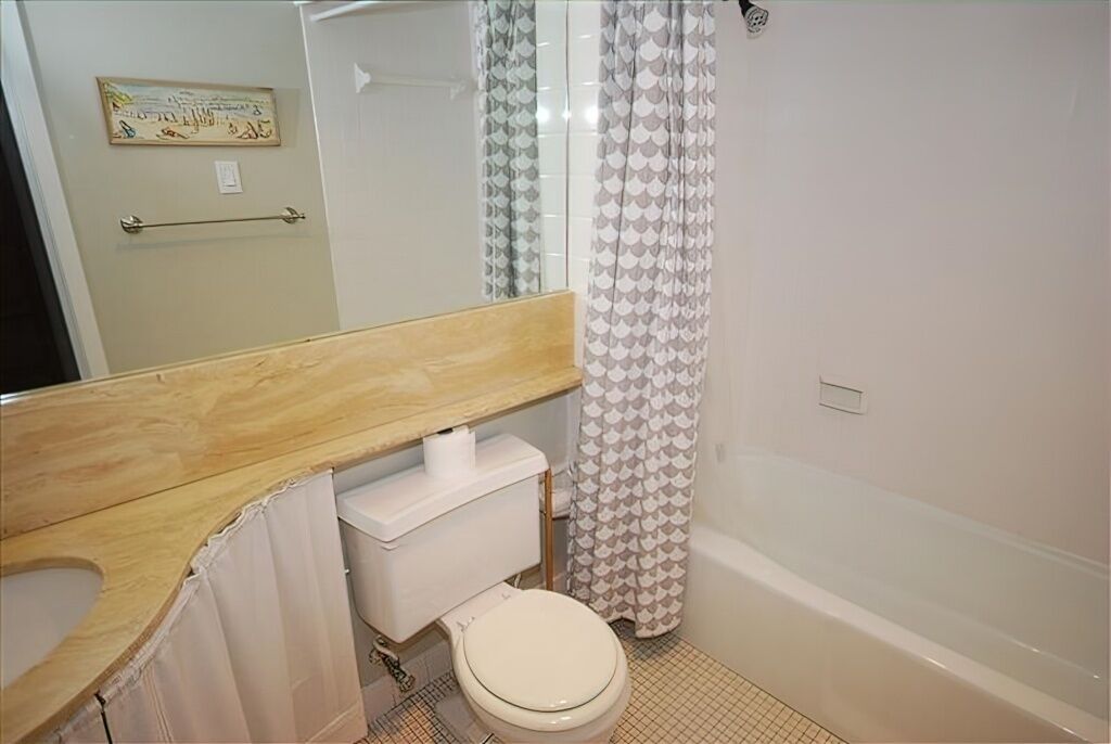 A bathroom with a wooden vanity, a toilet, a bathtub, and a shower curtain.