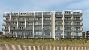 A multi-story hotel with balconies, a sandy foreground, and a clear sky. - Edgewater House - Ocean Front Units With Spectacular Views! (Rehoboth Beach)