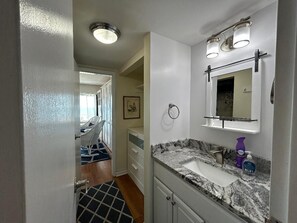 Ein Badezimmer mit Marmorplatte, Waschbecken, Spiegel und Duschbereich.