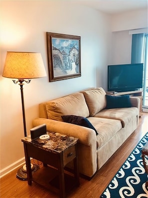 A living room with a beige sofa, a floor lamp, a framed artwork, a television, and a patterned rug.