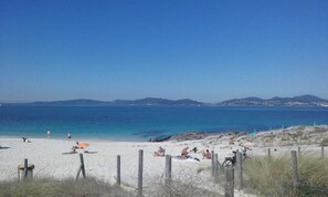 A beach with people sunbathing and swimming, a clear blue sky, and distant mountains.