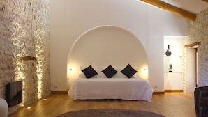 A bedroom with a stone wall, a white bed with black pillows, and a wooden floor.