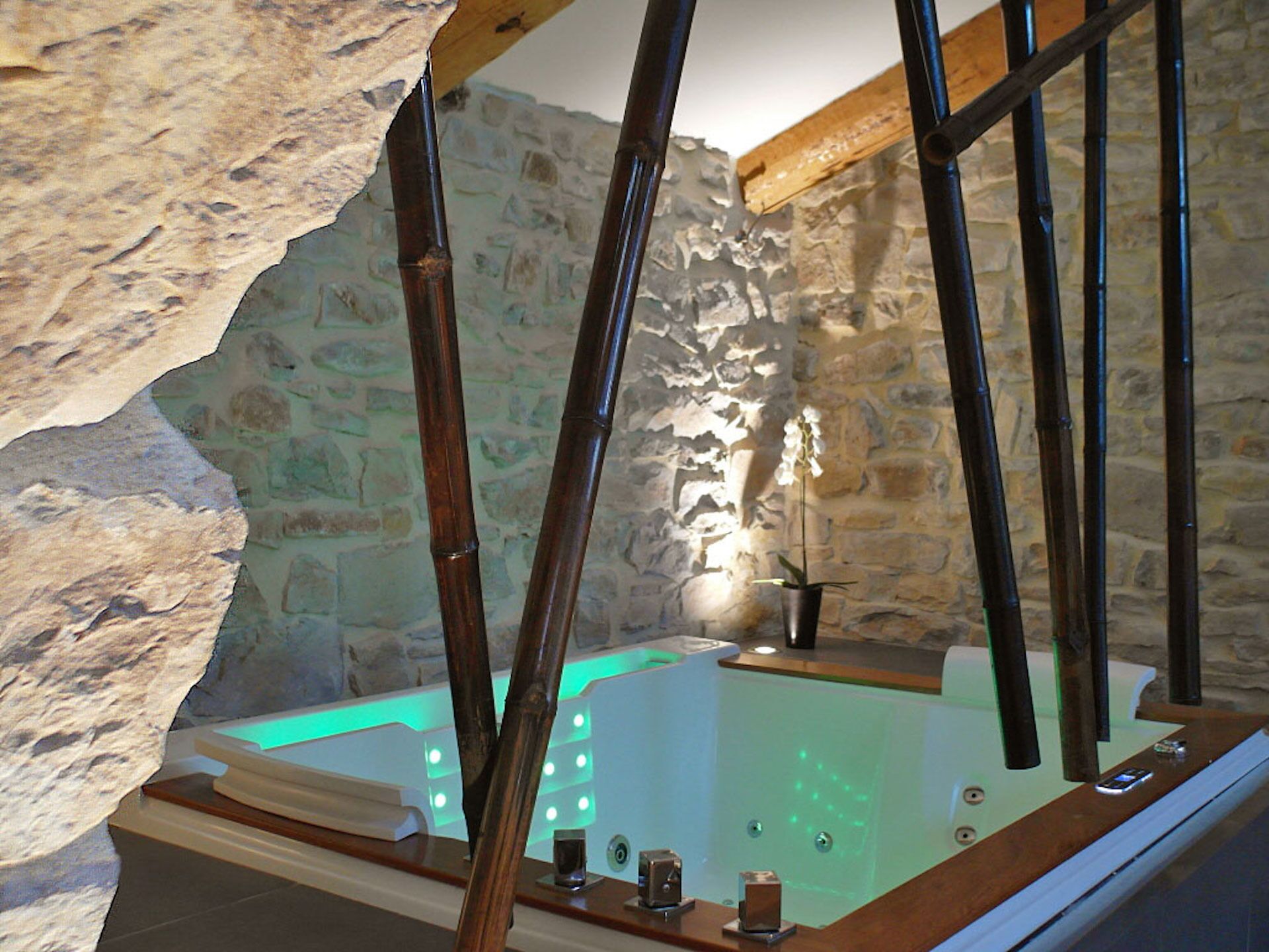 Ein Zimmer mit Steinwänden, einer Badewanne, Holzbalken und einem Topforchideen.