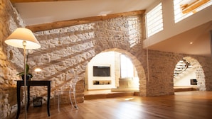 A spacious loft with exposed wooden beams, stone walls, and a large arched window.