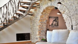 A modern living room with a stone wall, a white sofa, a wooden staircase, and a painting of a horse.