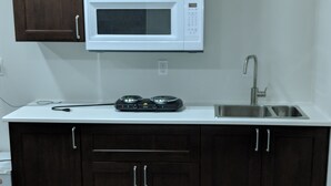 A kitchen with dark wooden cabinets, a white countertop, a microwave, a sink, and a stove. - Embassy Suites. (Winnipeg)