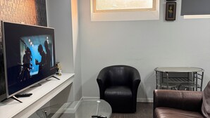 A modern living room with a flat-screen TV, leather furniture, a glass coffee table, and a small dining area with a metal chair. - Embassy Suites. (Winnipeg)