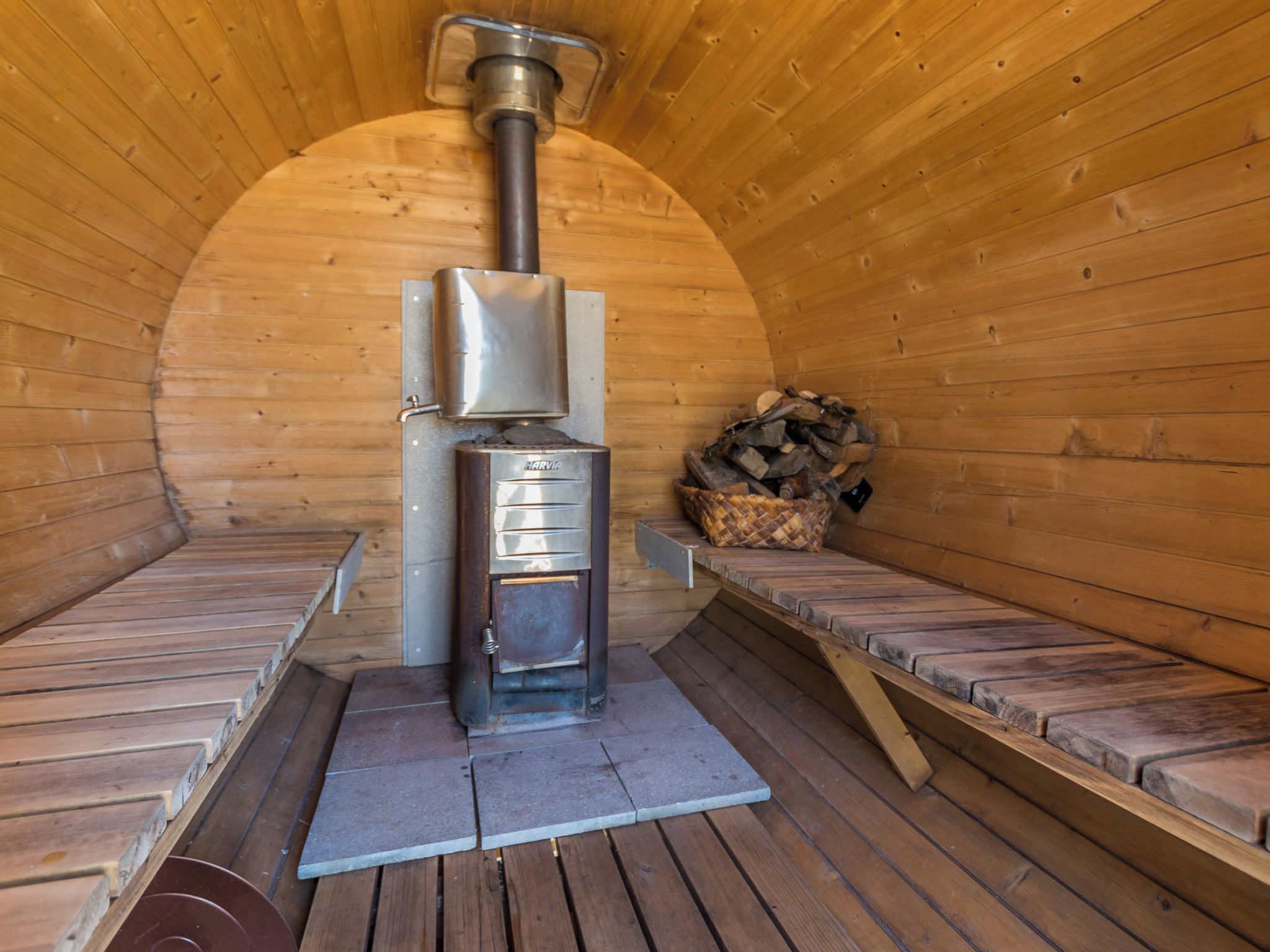 Un cuarto de sauna con estufa de leña, bancos y una pila de leña.