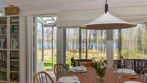 Comedor con una mesa dispuesta para seis personas, una estantería y vistas a un lago y árboles.