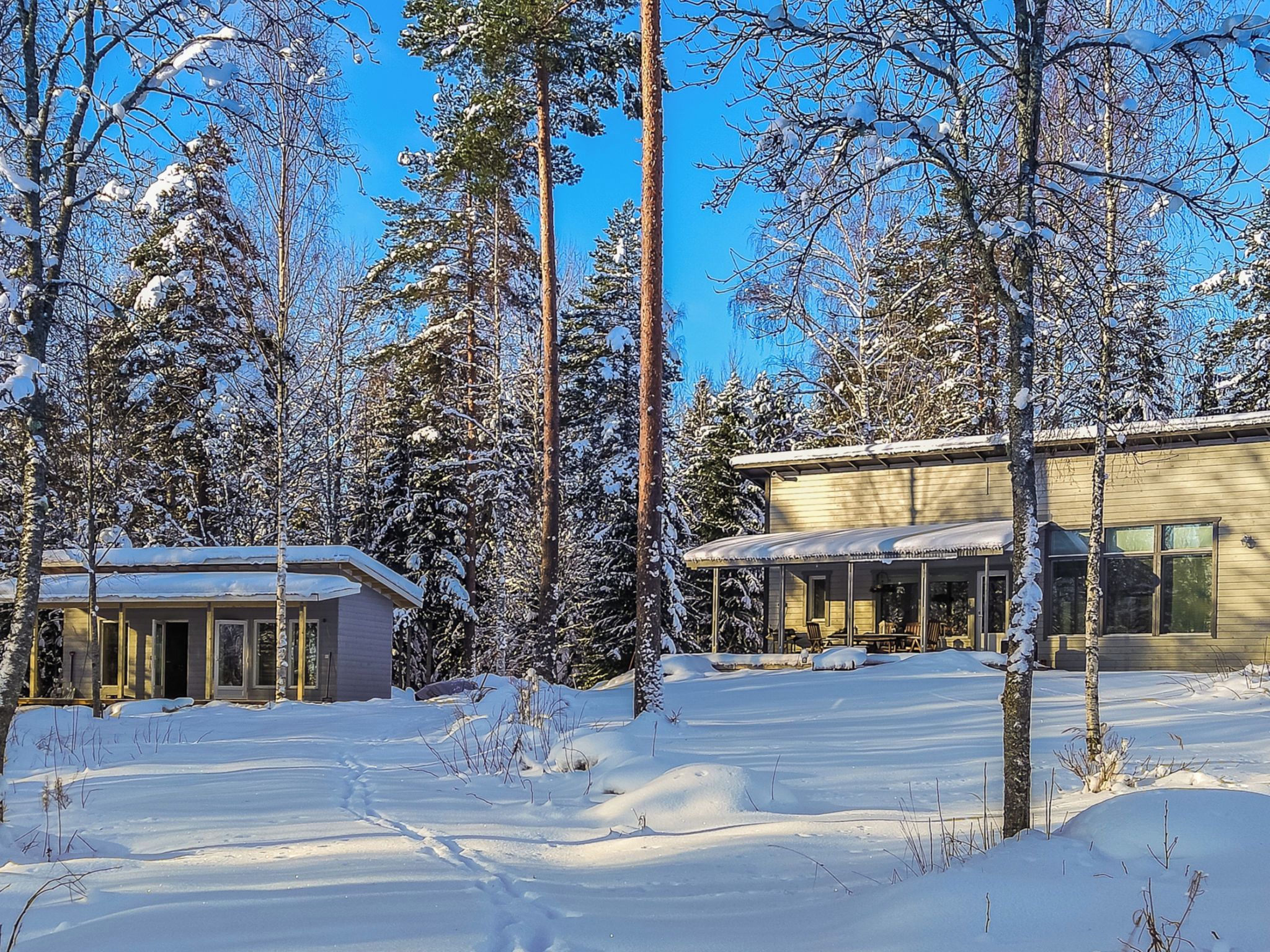 A snow-covered landscape with two buildings, one with a porch and another with a covered patio.
