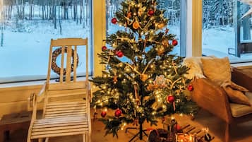 Una habitación acogedora con una silla de madera, un árbol de Navidad y vistas a un paisaje nevado a través de amplias ventanas.