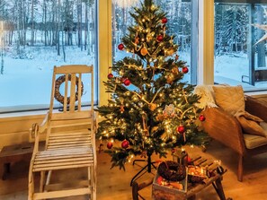 Una habitación acogedora con una silla de madera, un árbol de Navidad y vistas a un paisaje nevado a través de amplias ventanas.