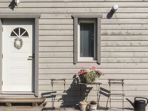 En bygning med hvide døre, et vindue med skodder og en veranda med bænke og en potteplante.