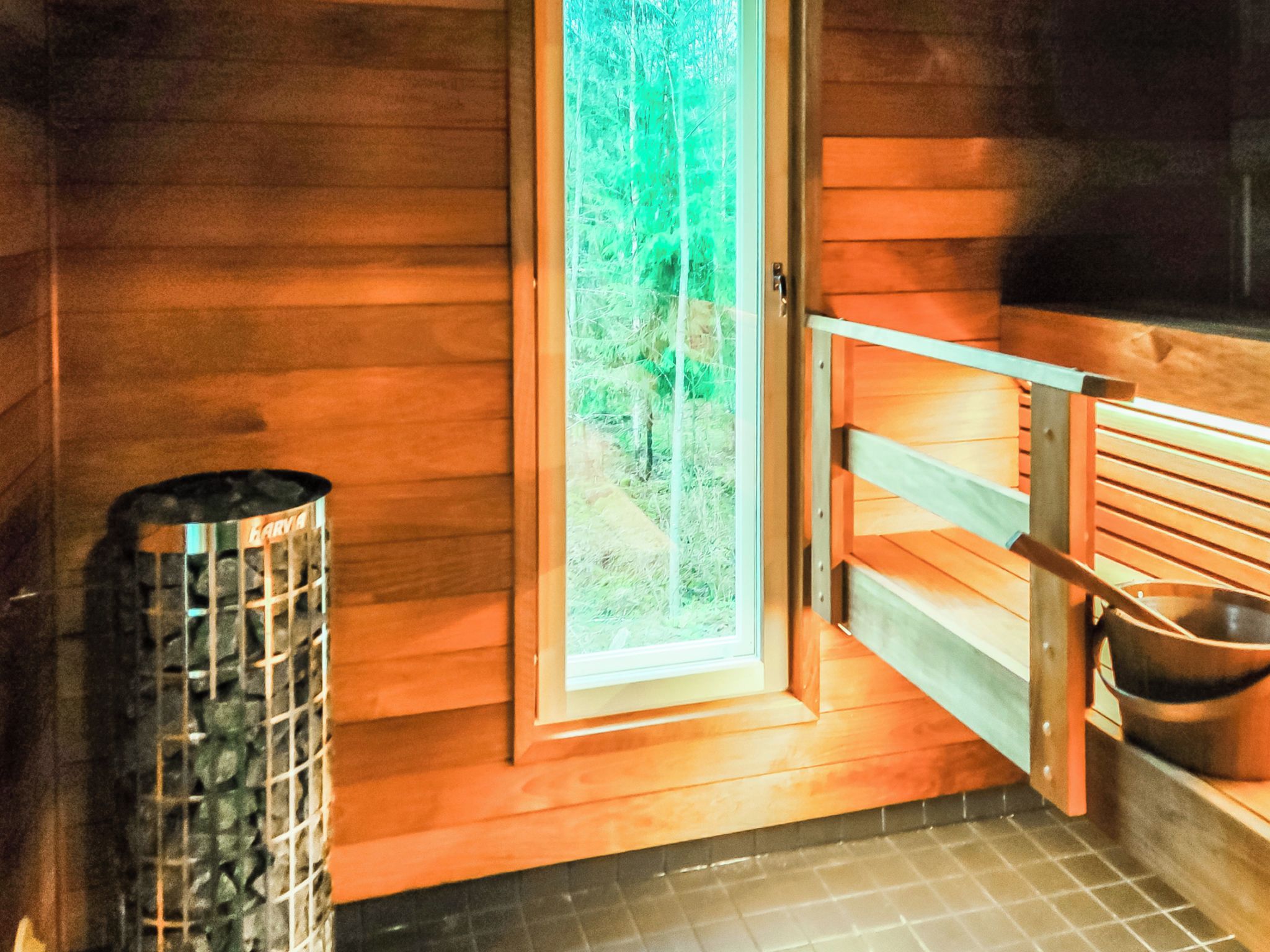 Un sauna con paredes de madera, puerta de vidrio, banco y un cesto de basura.