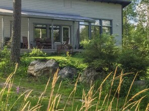 Moderni talo, jossa on katettu kuisti, suuret ikkunat sekä hyvin hoidettu puutarha, jossa on sekä kiviä että nurmikkoa.