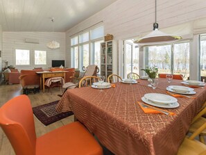 Un coin repas avec une table dressée pour quatre personnes, entourée de chaises orange, d’une bibliothèque et d’un téléviseur en arrière-plan.