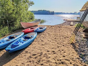 Une plage de sable avec des kayaks et un bateau, une clôture en bois et une forêt en arrière-plan.