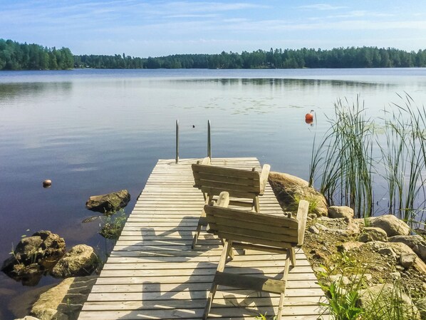Eine Holzstege führt in einen ruhigen See, mit einer Bank und einem Bojen.
