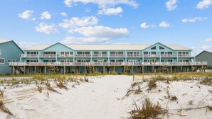 Um hotel à beira-mar com fachada azul clara, várias varandas e uma praia de areia em frente.
