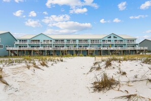 Un hôtel situé en bord de mer, avec une façade bleu clair, de nombreux balcons et une plage de sable devant.