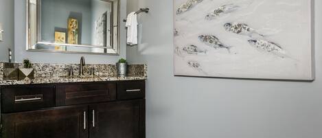 A bathroom with dark wooden cabinets, a granite countertop, a large mirror, and a wall-mounted artwork of fish.