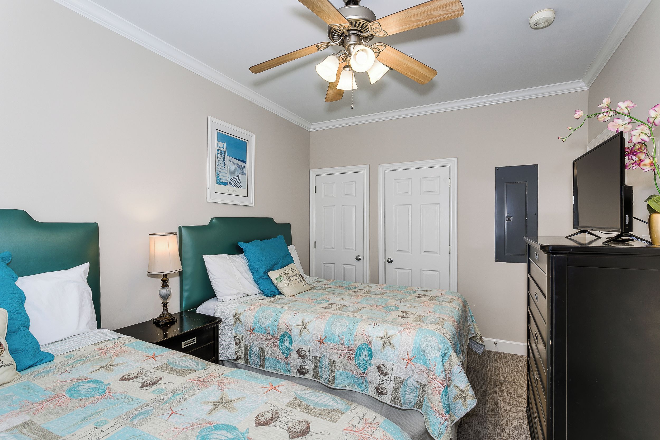A bedroom with two beds, a ceiling fan, a dresser, and a TV.